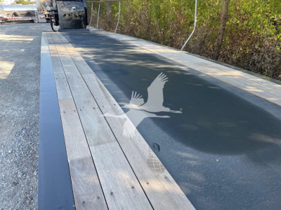 Trailer deck showing wooden planks and metal edge on a 2024 XL Specialized Mini Deck trailer, with an engraved logo visible on the surface.