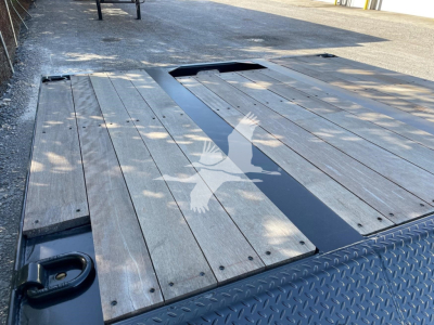 Trailer deck showing wooden planks with metal edge and side rails, rear cutouts for ramps, and a Diamond plate fender in foreground.