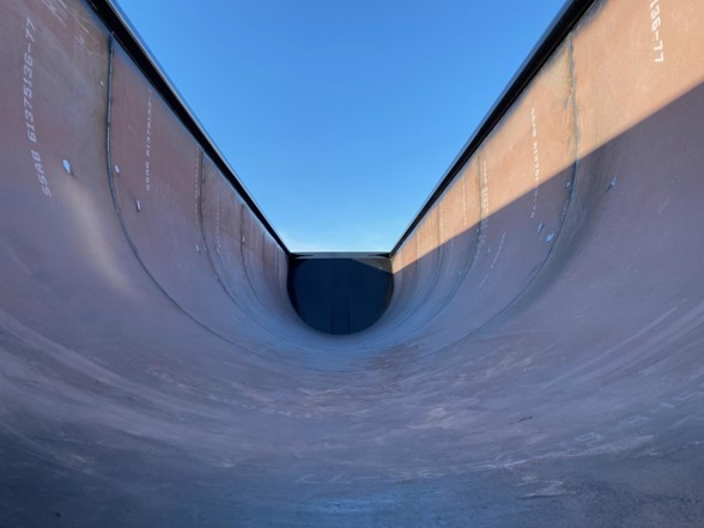 Large dump trailer bed interior with curved walls, showing metal surfaces and a dark transition at the bottom. No readable text visible on the image.