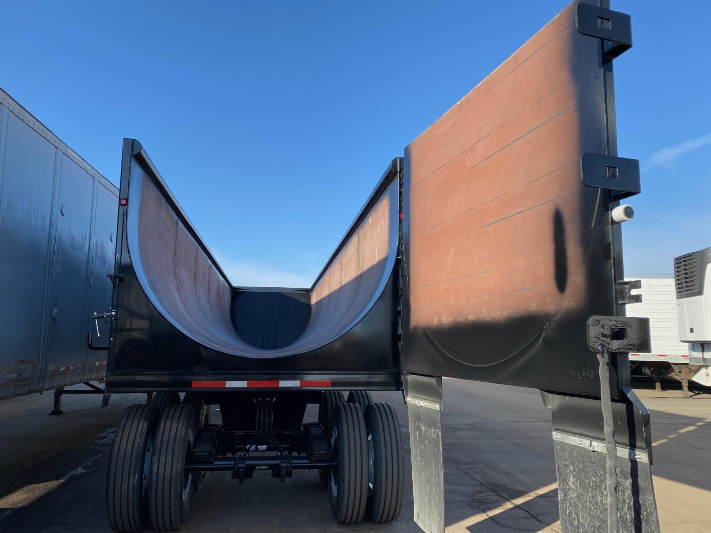 Dump trailer bed showing elevated sides and dual rear axles with black undercarriage and open-top cargo area.