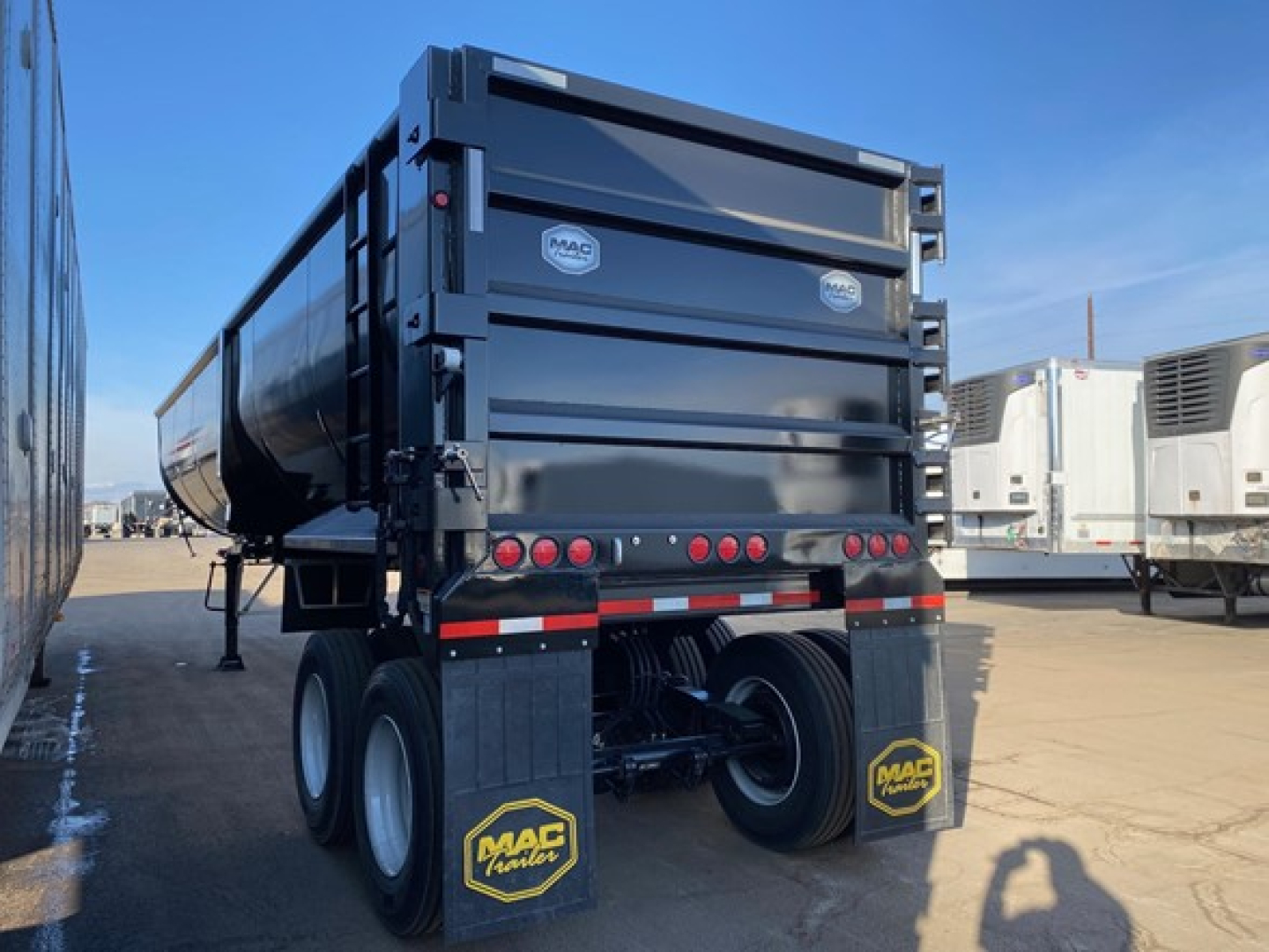 Mac Scrap trailer rear view showing dump trailer with MAC logo decals, taillights, mud flaps, dual rear wheels, and support legs.