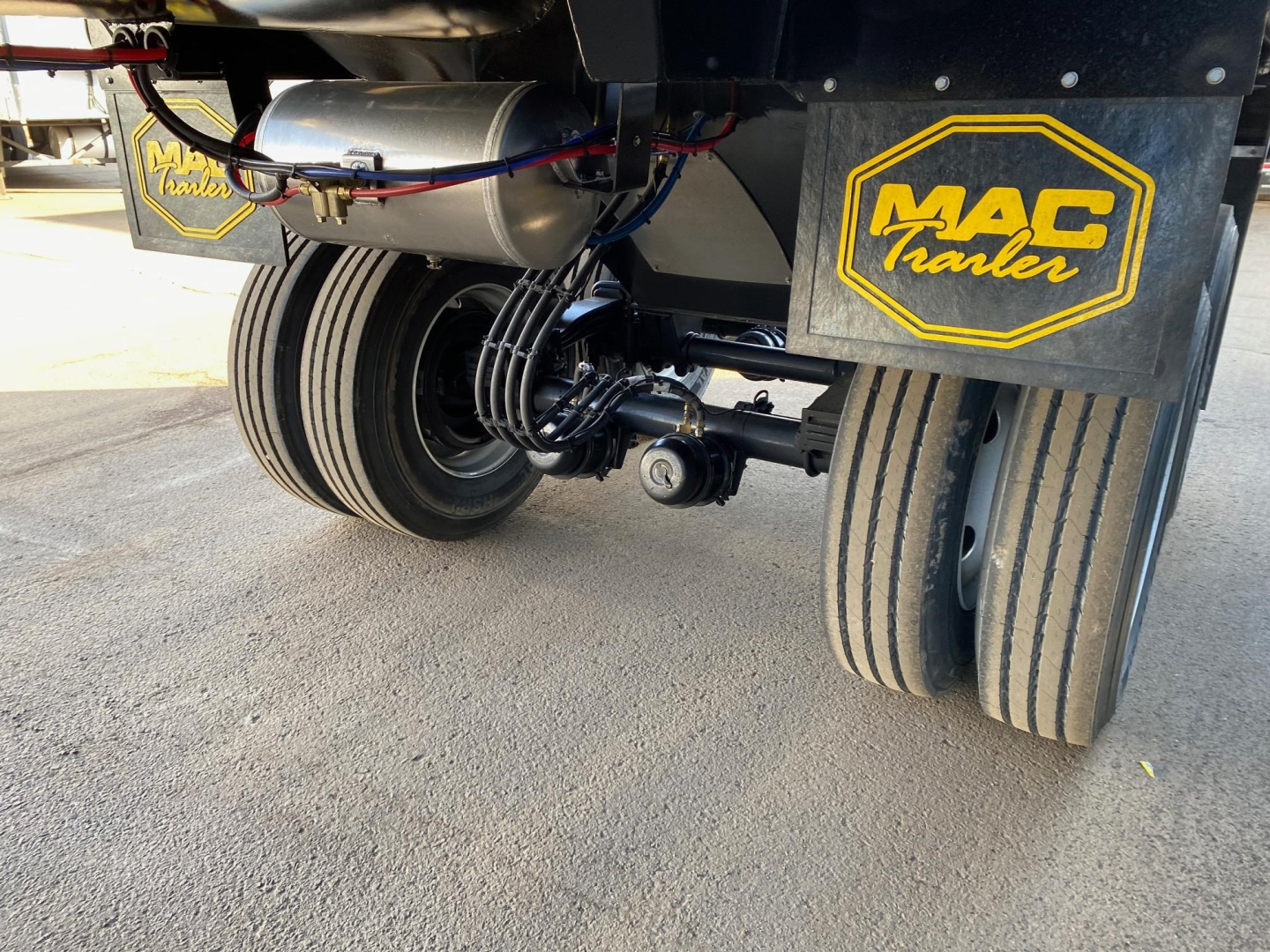 Mac Trailers dual-tandem rear dump trailer wheels and axle assembly with MAC Trailer logo on mudflaps.