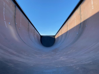 Large dump trailer bed interior with curved walls, showing metal surfaces and a dark transition at the bottom. No readable text visible on the image.