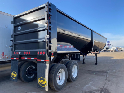 Dump trailer with black steel body and dual rear axles showing Mac trailer mudflaps and reflective tape.
