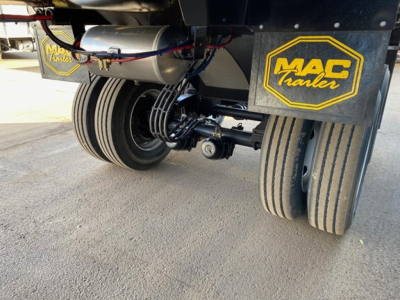 Trailer rear undercarriage showing dual axles with Mac Trailers branding on mud flaps and hydraulic lines above", component text: MAC trailer logo on yellow and black mud flaps.