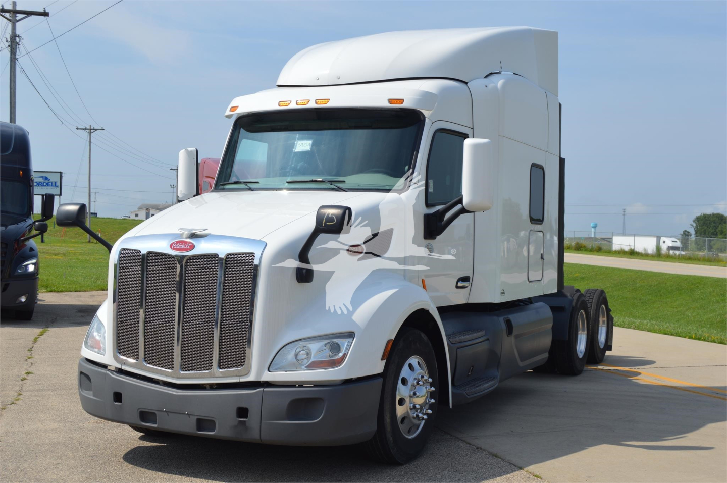 Peterbilt 579 conventional sleeper truck in white, front left view with grille and aerodynamic cab, showing large chrome bumper and dual rear axles.