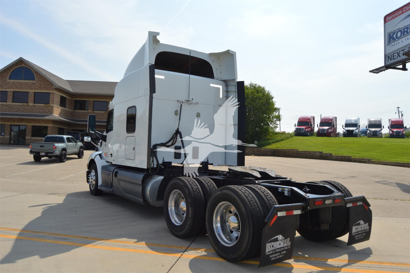 Peterbilt 579 tractor-trailer cab from rear-left view showing dual rear axles and fifth wheel, with white cab and chrome wheels.
