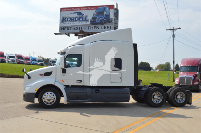 Peterbilt 579 conventional sleeper truck side view showing cab and tandem rear axles with white paint and decorative logo.