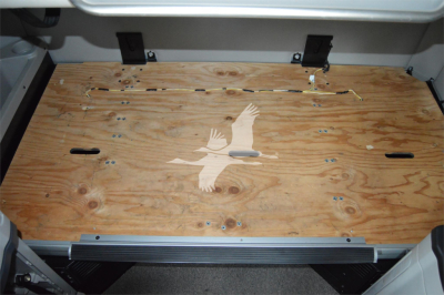 Truck cargo area showing plywood bed with a bird graphic and metal latches along top edge; interior side walls visible