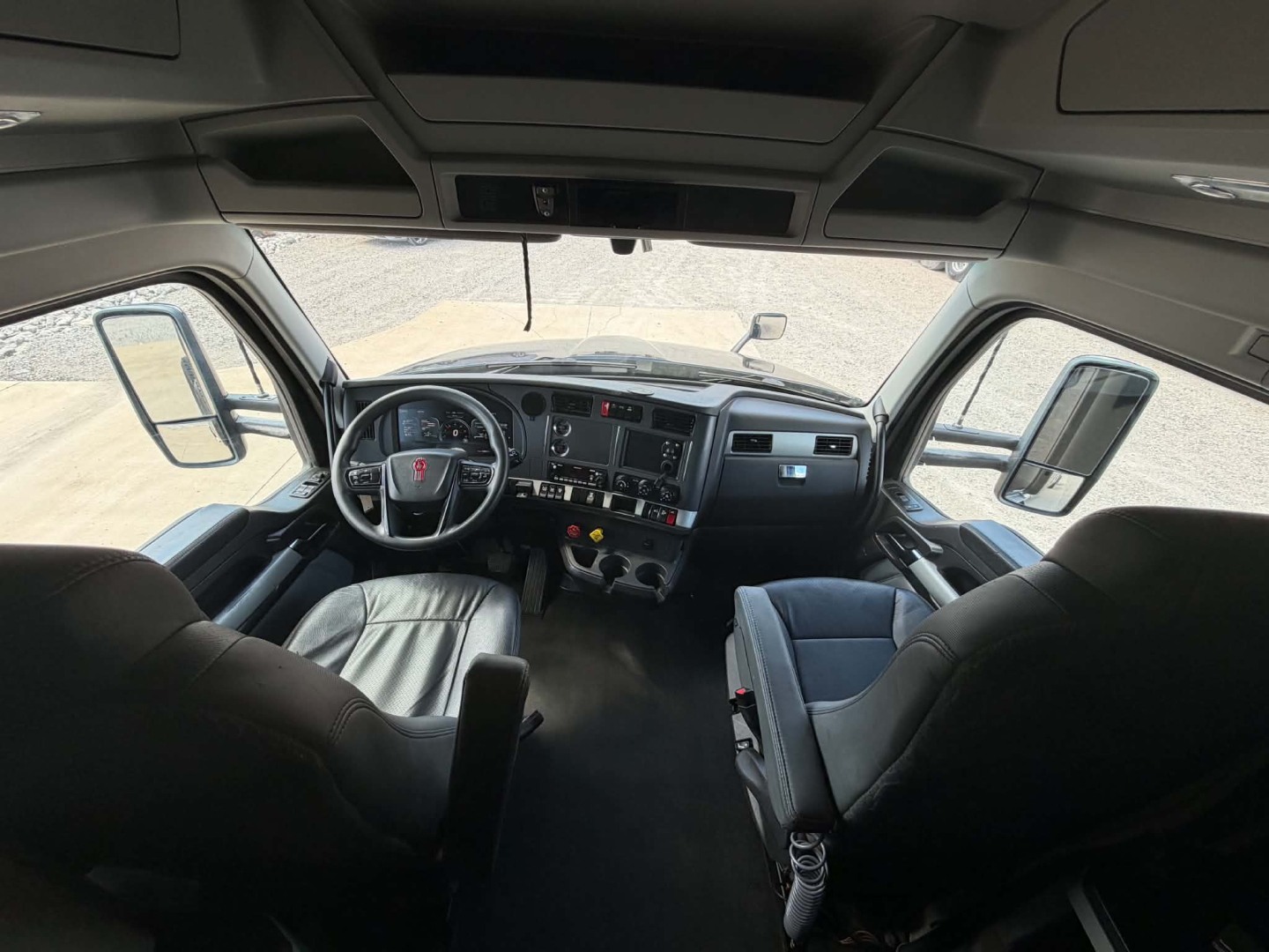 Kenworth T680 truck cab interior showing steering wheel, dashboard with gauges, center control panel, and driver and passenger seats.