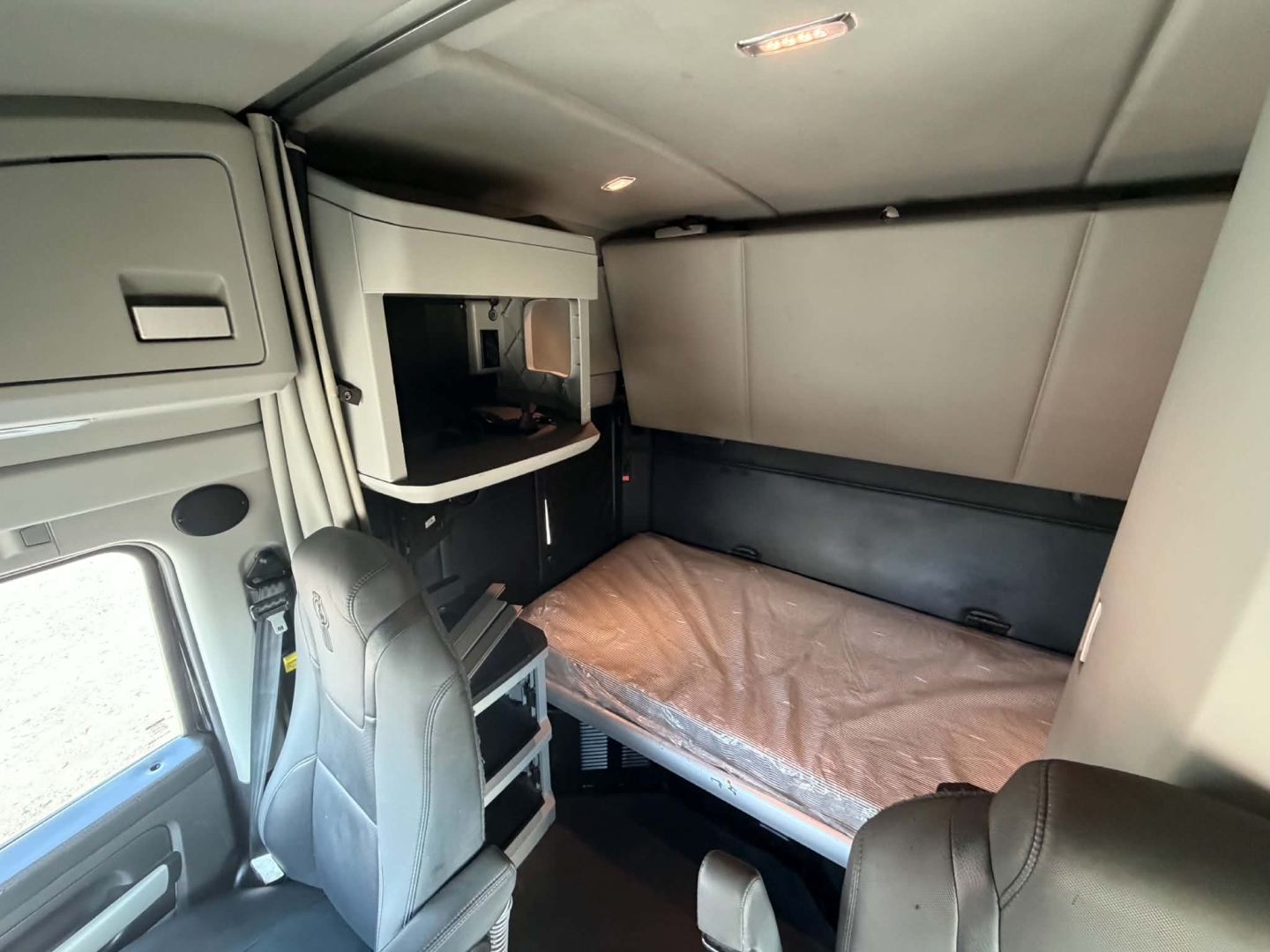 Kenworth T680 sleeper cab interior showing bunk bed, storage shelf, and seating area.