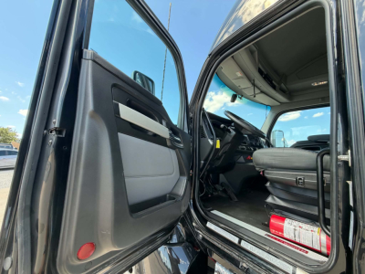 Kenworth T680 cab interior and open door showing steering wheel, driver's seat, and entry area with a fire extinguisher on the floor, view into cabin