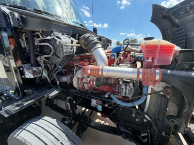 Kenworth T680 engine bay visible with red engine, coolant reservoir, hoses, and intake piping.