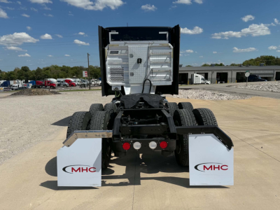 Kenworth T680 rear view showing fifth wheel area and mud flaps with MHC logos, dual rear axles, chrome fuel tanks visible, clear sky