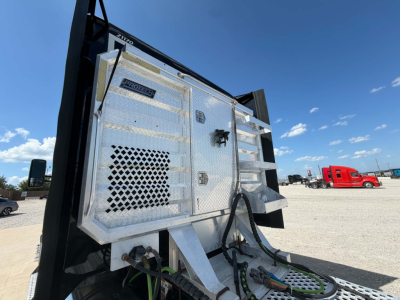 Truck body side with a diamond-plate aluminum toolbox mounted on a Kenworth T680, with black hydraulic lines and hoses, and a perforated panel. Clear blue sky.