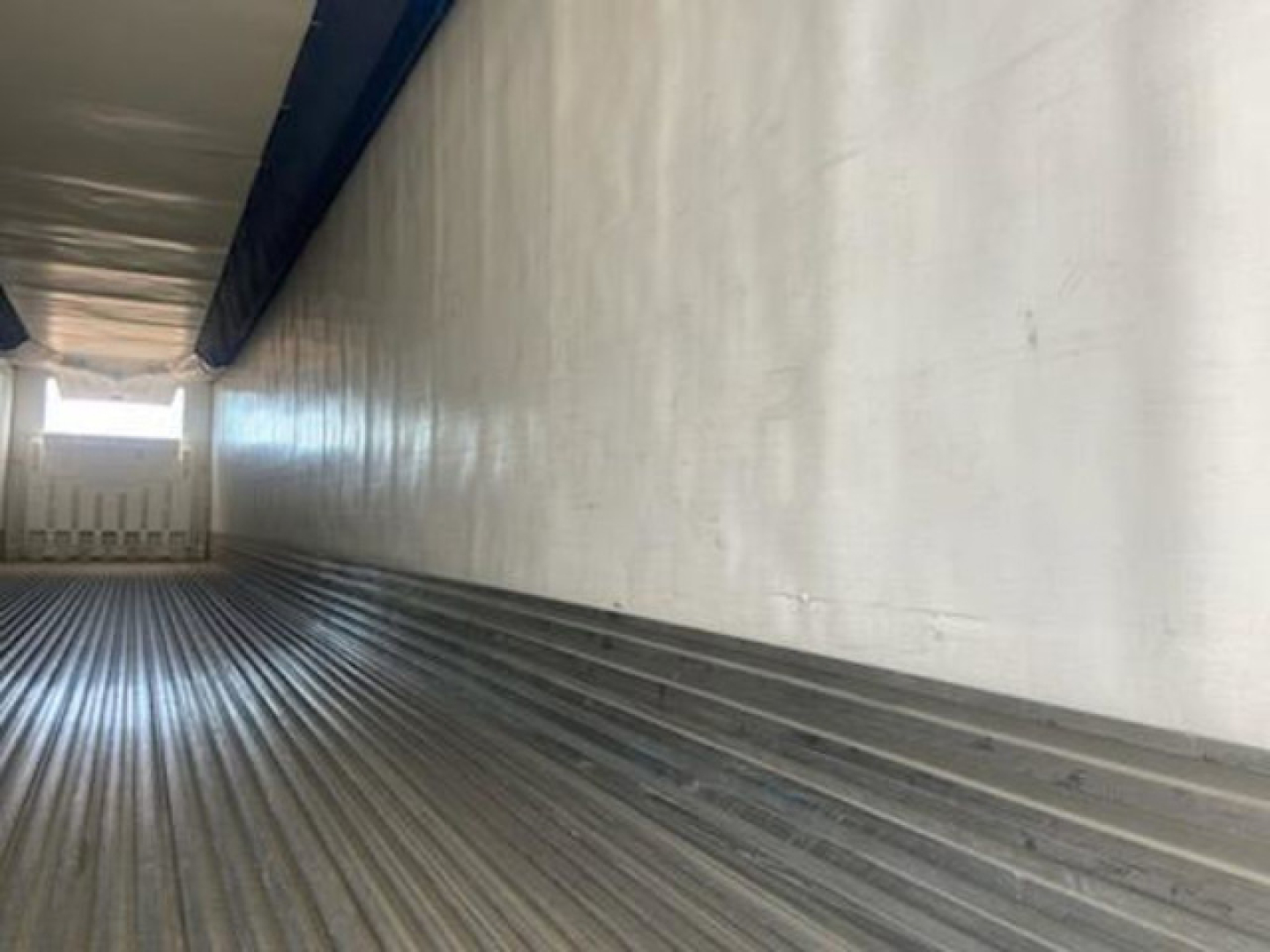 Trailer interior showing corrugated metal floor with ribs and white side walls; rear doorway visible at far end.