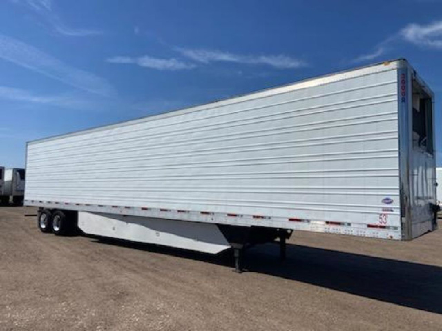 Trailer side view showing a white refrigerated utility trailer with ribbed aluminum siding and tandem axles.