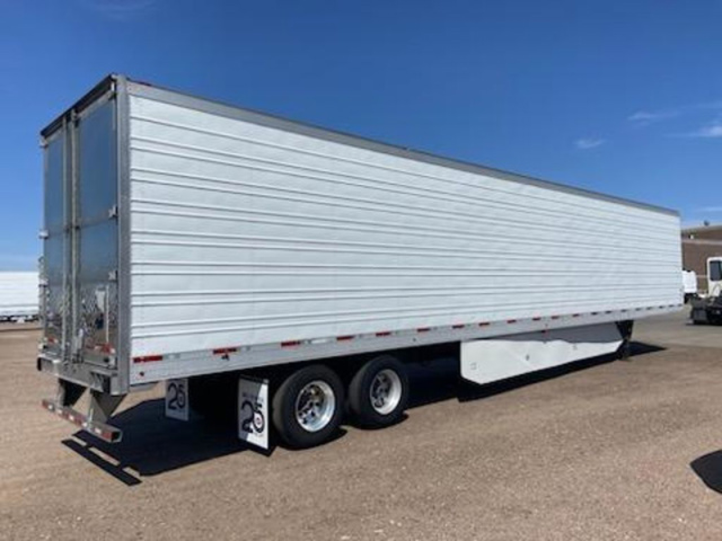 Tri-axle refrigerated trailer with white aluminum sides shown in a parking lot.