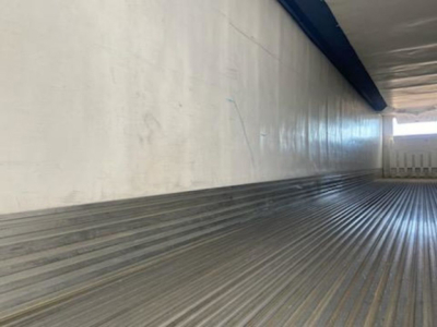 Trailer interior: corrugated metal floor and side walls of a refrigerated trailer interior, light entering from opening at far end.