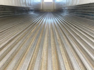 Trailer interior showing ribbed metal floor and side walls, rear door opening, light at far end.