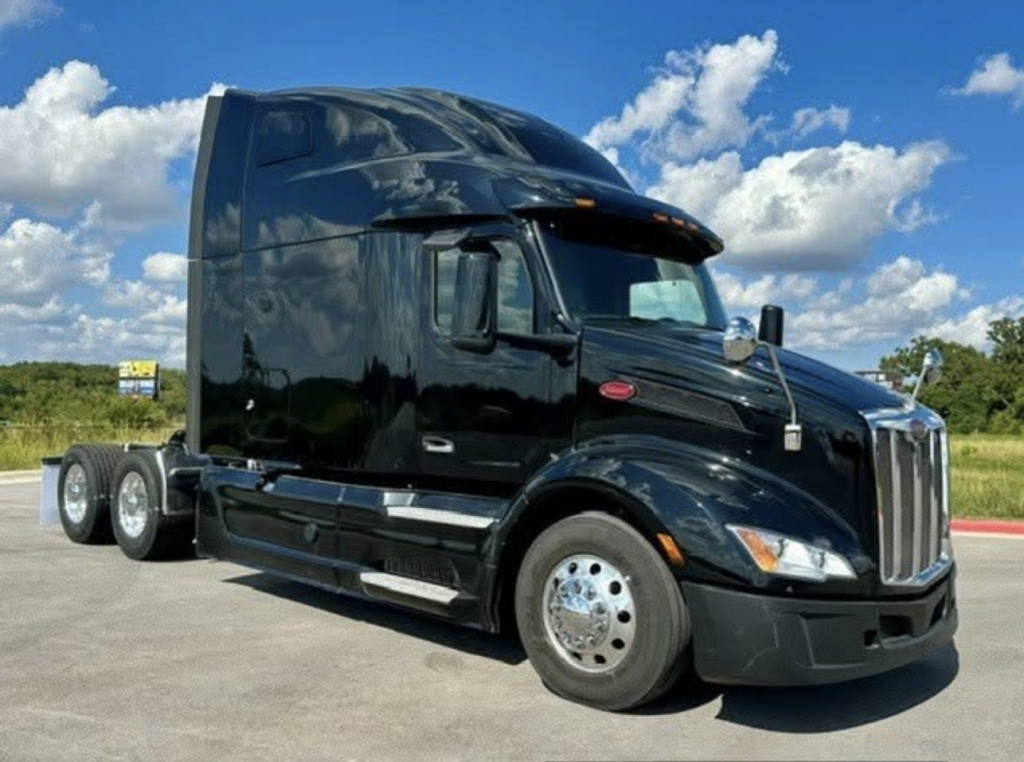 Peterbilt 579 tractor unit in black, side view showing sleeper cab, dual rear axles, chrome rims, and daytime running lights.