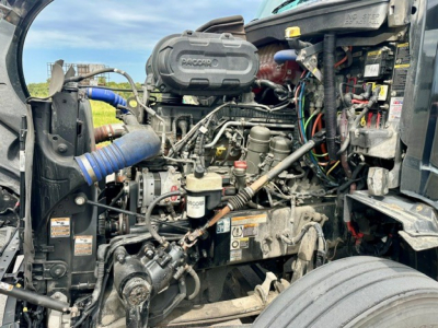 Peterbilt 579 engine bay showing Cummins/Detroit-style engine with RACOR fuel filter and various hoses and wiring visible.
