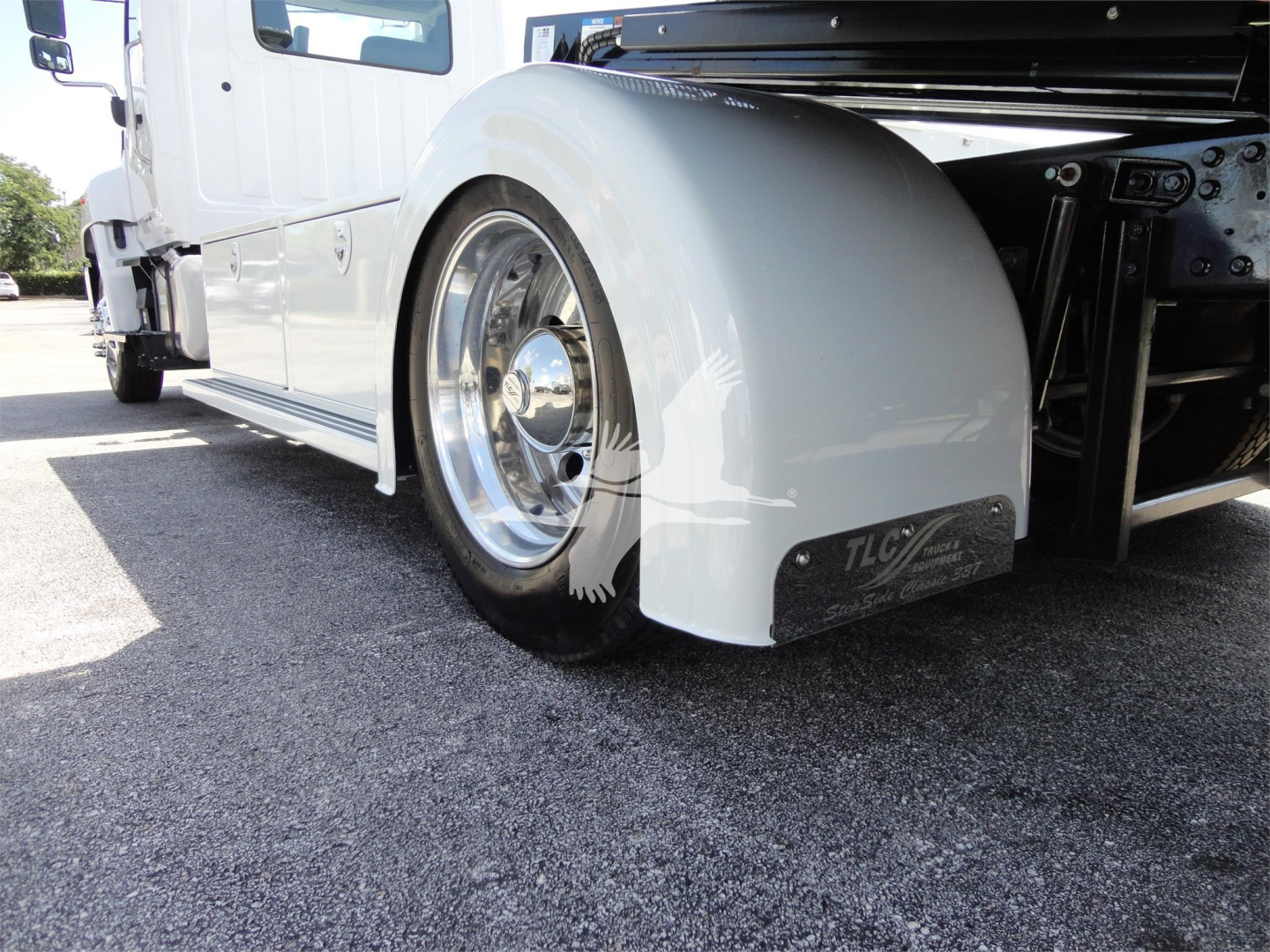 Truck rear wheel and fender on a 2022 Hino 268A rollback, chrome wheel, white body, black mudguard with TLC sticker, side view showing wheel well and chassis