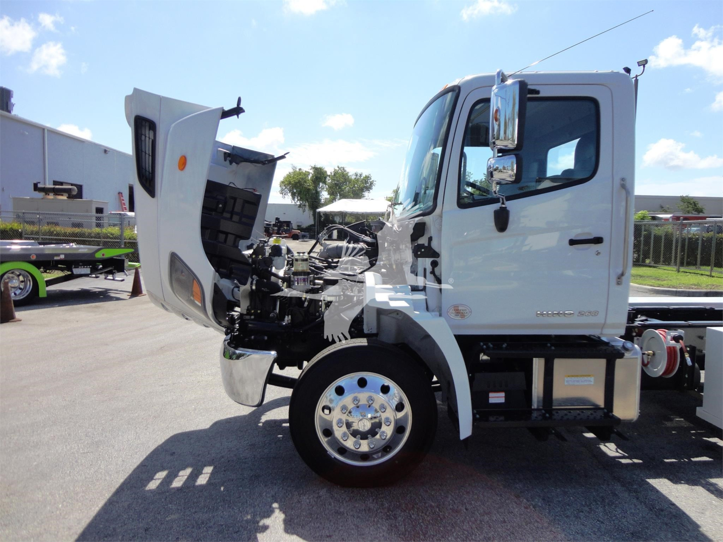 Rear-slash side view of a white 2022 Hino 268A rollback truck with hood open, showing engine bay and front wheel, cab doors visible.