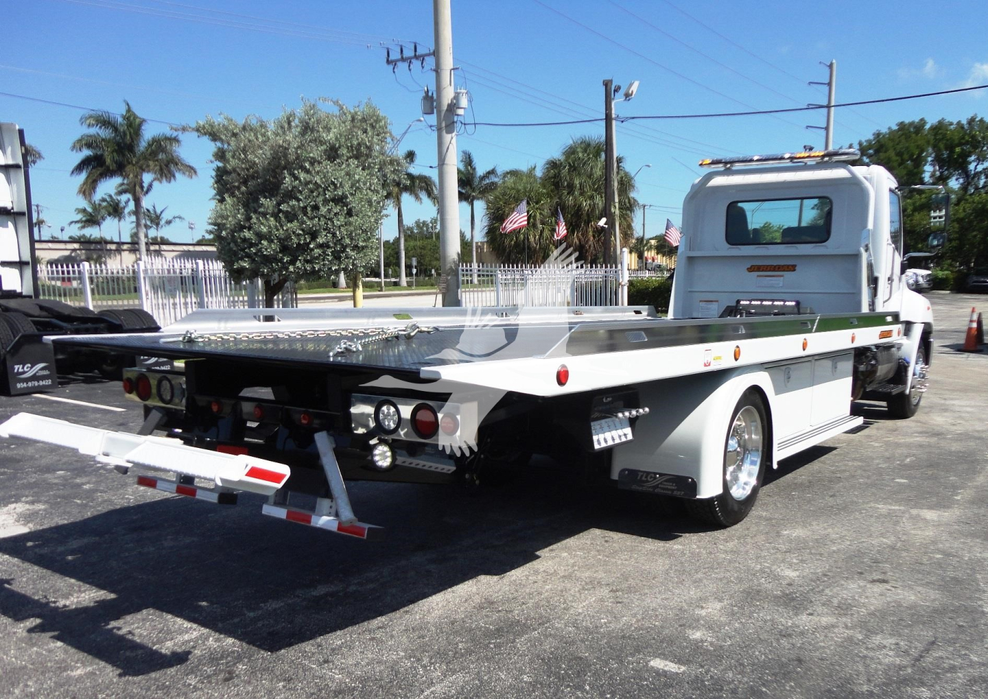 Rear and side view of a white 2022 Hino 268A rollback tow truck with a flatbed, dual rear lights, and metal side rails.