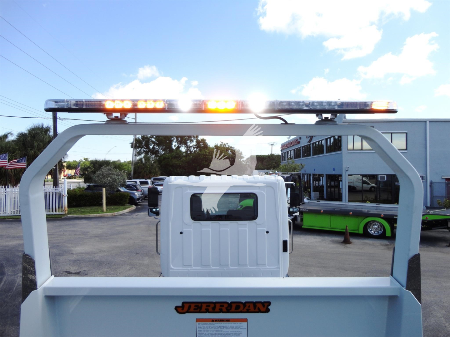 Front view of a 2022 Hino 268A rollback truck cab and rear cargo bed with orange emergency lights on top of the frame.