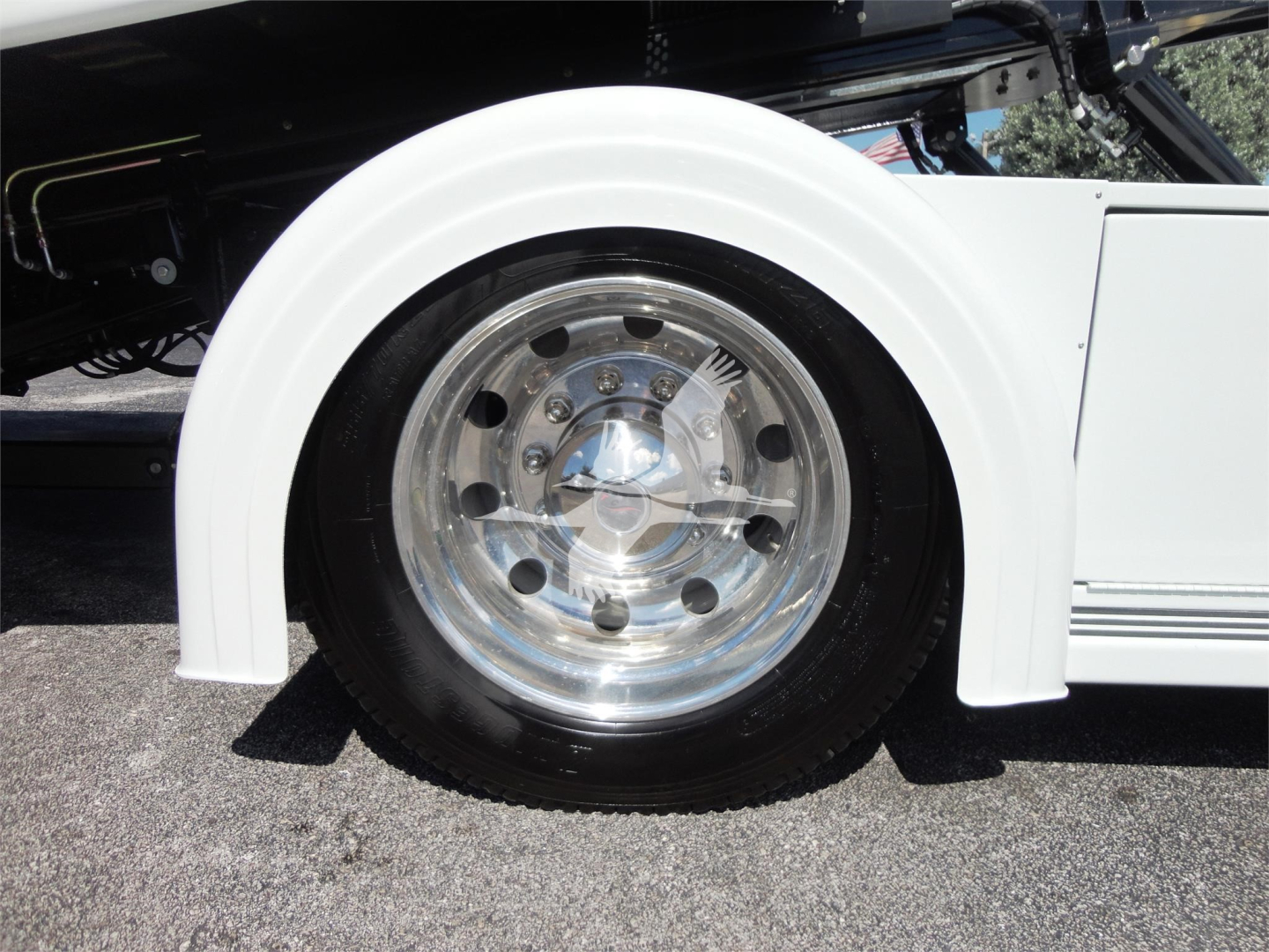 Wheel with chrome hubcap and white fender of a truck, partial view of suspension and body lines.