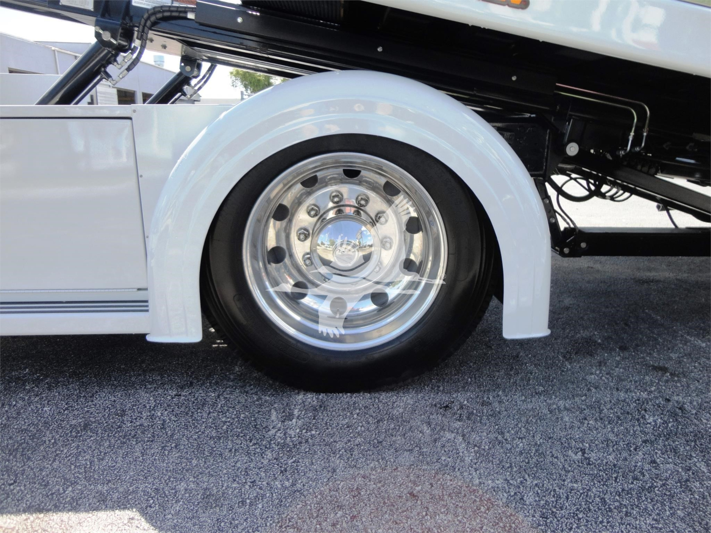 Truck wheel well and chrome wheel on a 2022 Hino 268A rollback truck showing white fender and partial undercarriage.