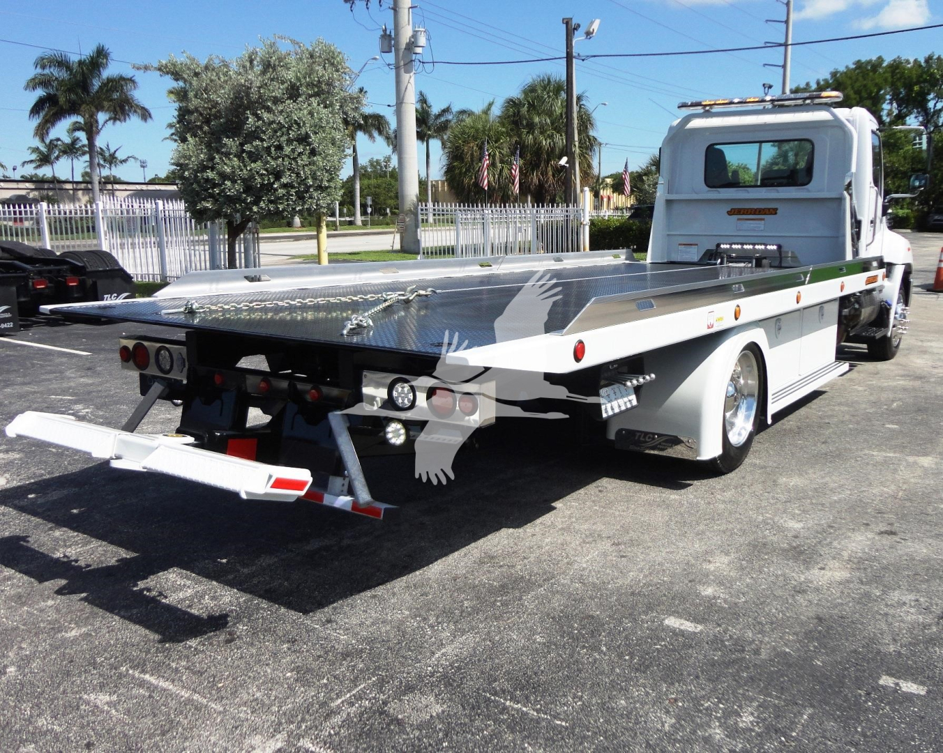 Flatbed tow truck in a commercial lot, side view showing long aluminum flatbed and rear underride bumper.