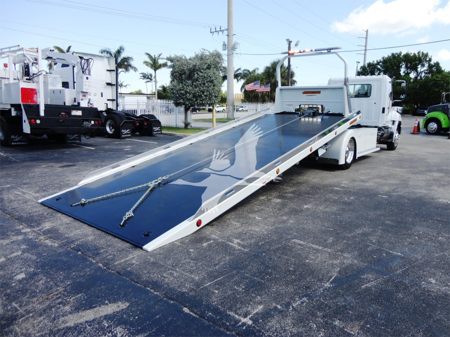 Truck with a lowered flatbed tow truck body showing a hydraulic ramp and tie-down chains.