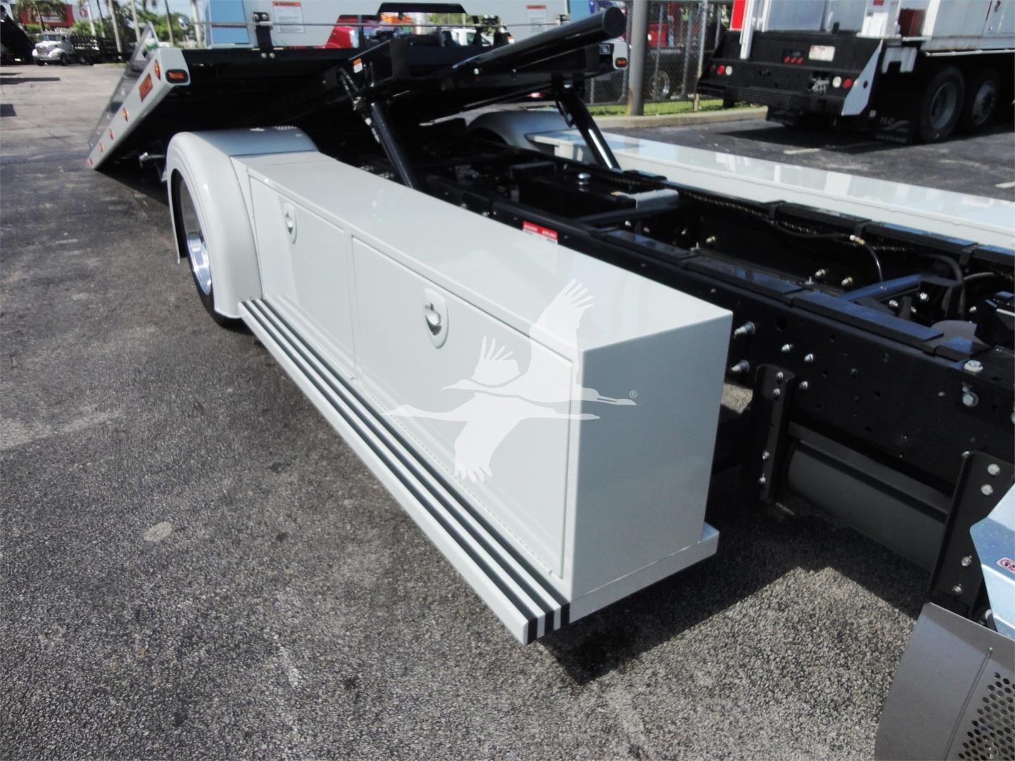 Hino 268A rollback truck side view showing white storage box with horizontal black stripes and hydraulic chassis components.