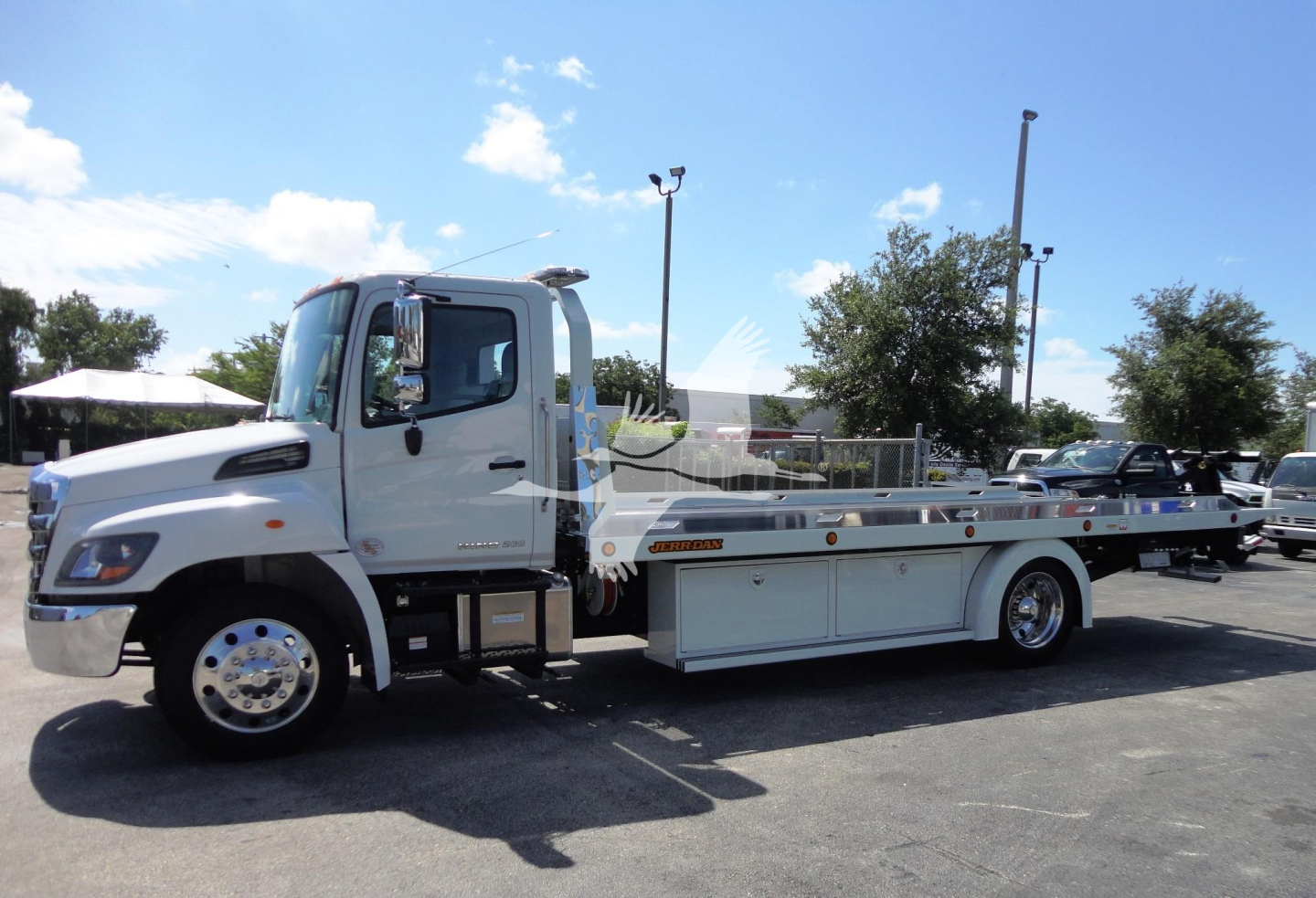 Hino 268A rollback tow truck side view showing flatbed with storage compartments and white cab.