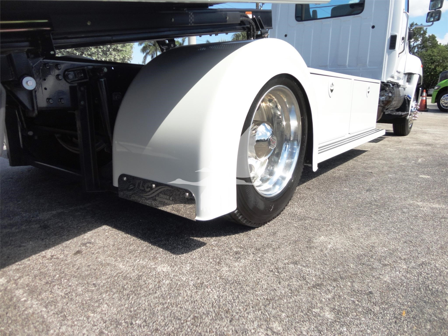 Truck wheel arch and front fender of a white Hino 268A rollback truck with chrome wheel cover and fender.