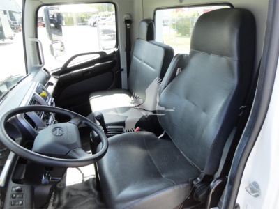 Truck cab interior showing steering wheel and two black vinyl seats; dashboard with controls; front passenger seat visible.