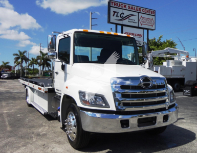 Front-left view of a white 2022 Hino 268A rollback truck with chrome grille and bumper, flatbed wheel-lift, and large side mirrors.