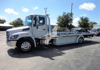 Truck body showing a white 2022 Hino 268A rollback w/ long flatbed and equipment racks.