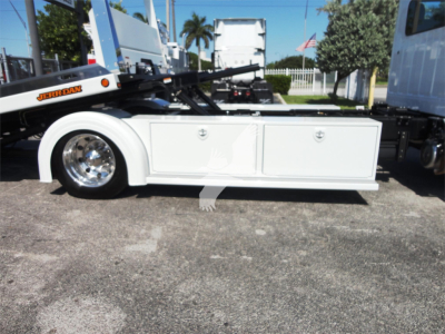 Side view of a 2022 Hino 268A rollback truck showing a white storage toolbox and wheel with chrome rim.