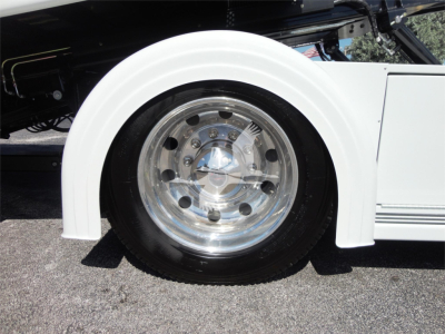 Wheel with chrome hubcap and white fender of a truck, partial view of suspension and body lines.