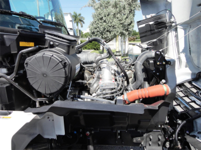 Truck engine bay of a 2022 Hino 268A rollback showing air intake, hoses, and engine components with orange coolant hose.