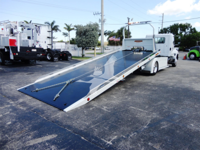 Truck with a lowered flatbed tow truck body showing a hydraulic ramp and tie-down chains.