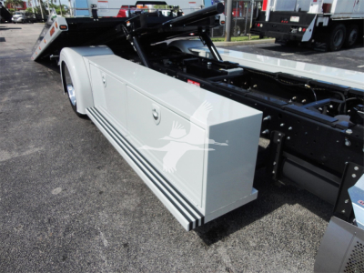 Hino 268A rollback truck side view showing white storage box with horizontal black stripes and hydraulic chassis components.
