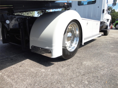 Truck wheel arch and front fender of a white Hino 268A rollback truck with chrome wheel cover and fender.