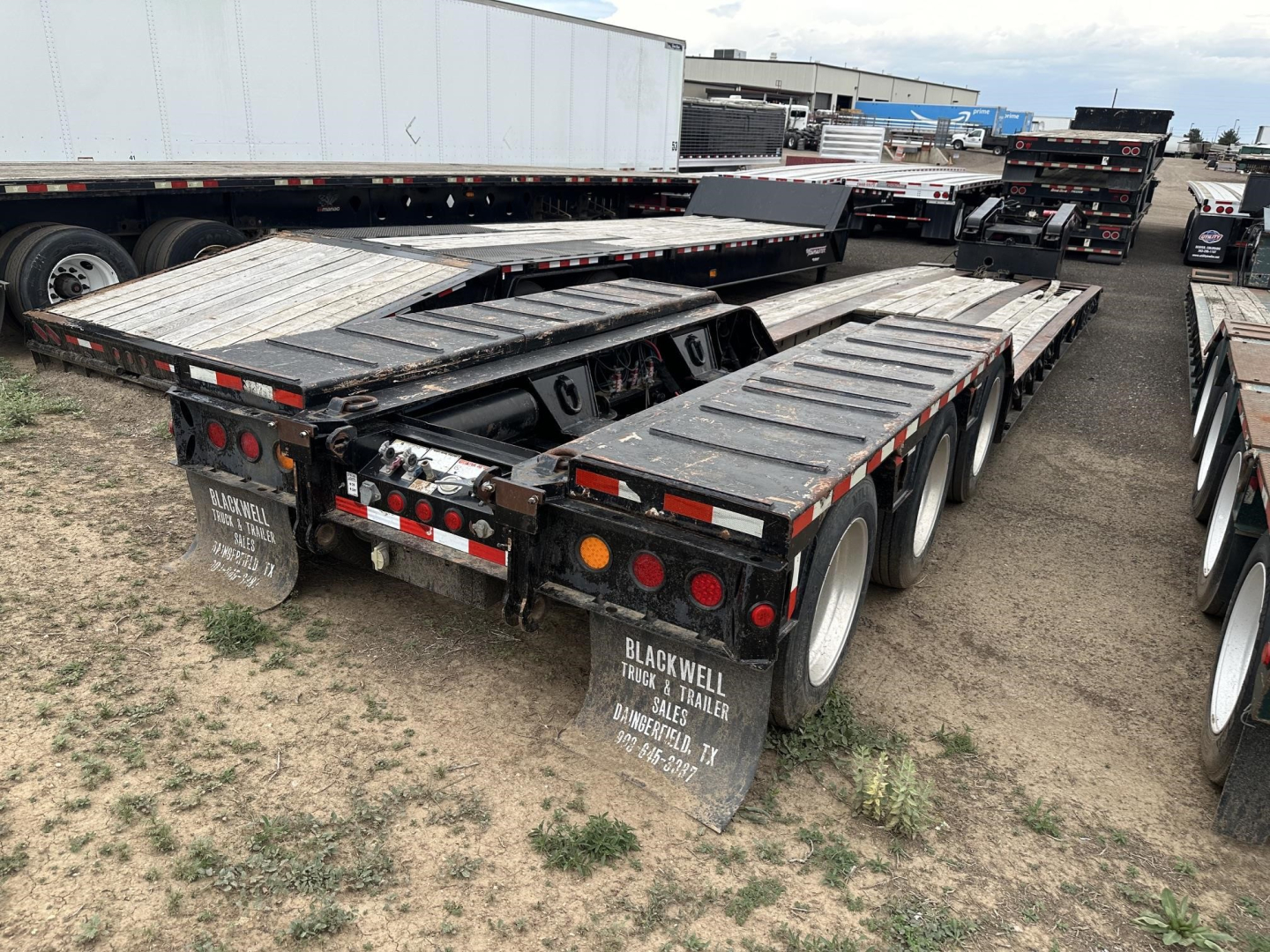 Load King lowboy trailer in a yard showing rear and side ramps, multiple axles, and mudflaps with service markings.