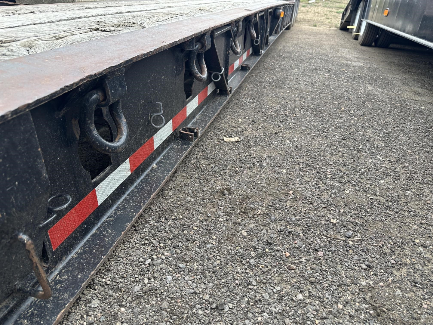 Lowboy trailer edge showing hooks and reflective red/white stripe along the side, from a ground-level view.