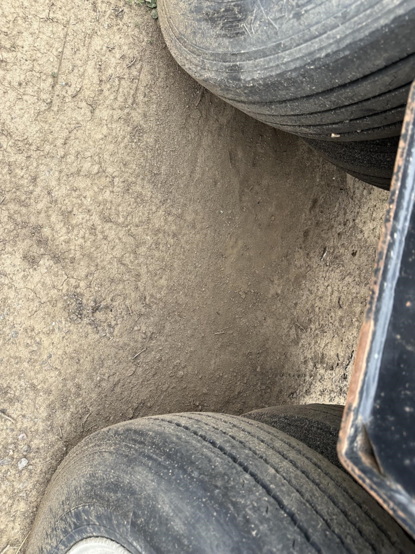 Lowboy trailer wheel area showing dual tires and dirt on mud surface, loading deck edge and suspension components visible.