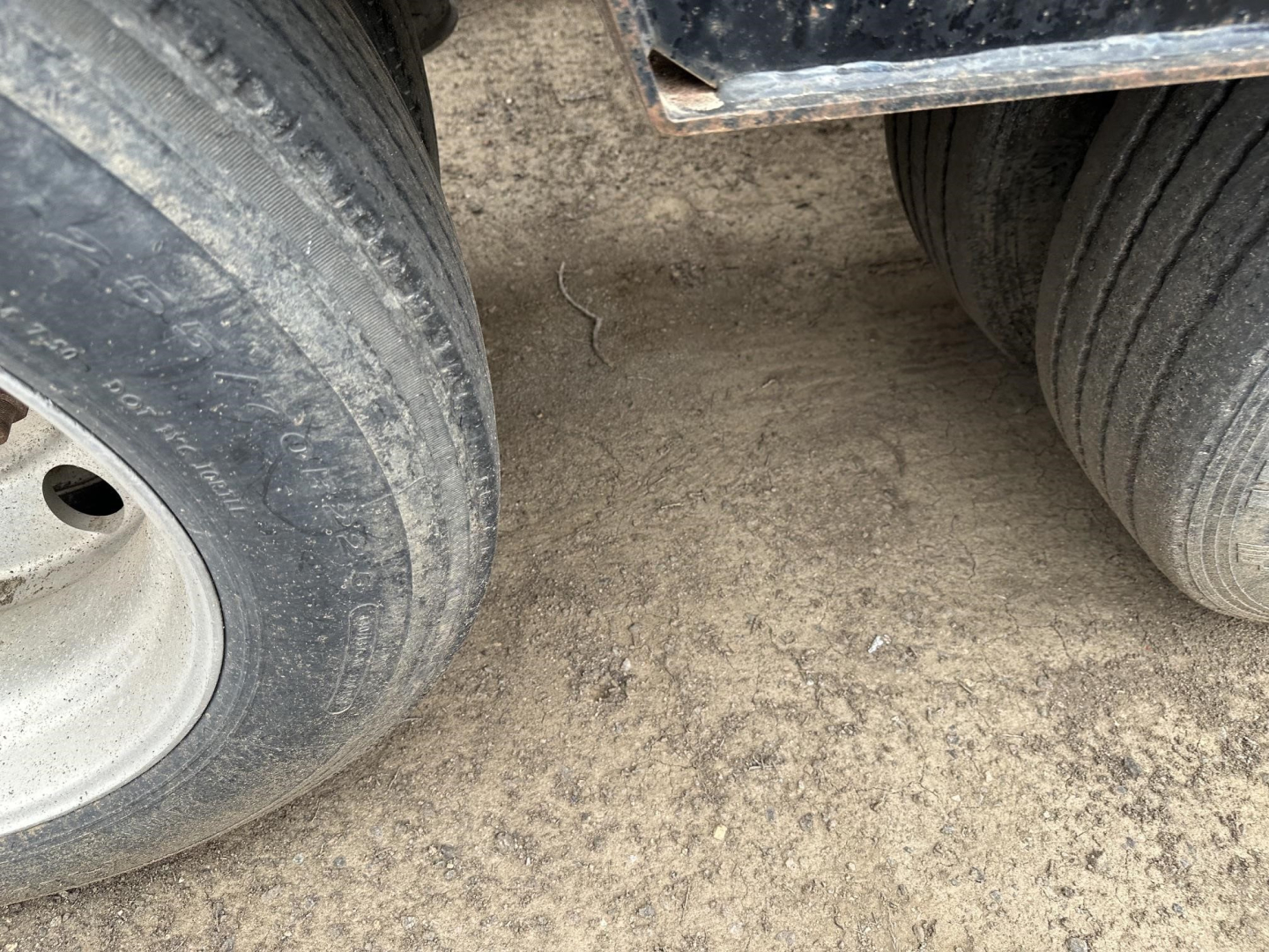 Lowboy trailer wheel tread and muddy ground with dual tires visible under trailer frame.